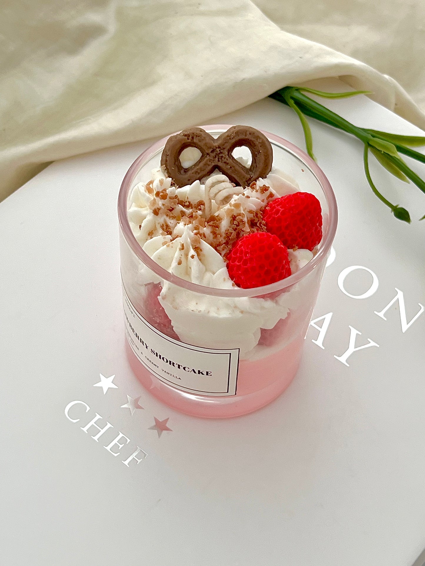 Handmade Strawberry Shortcake dessert candle in a clear glass jar with whipped wax topping, vibrant red wax strawberries, and chocolate detail, styled on a white background